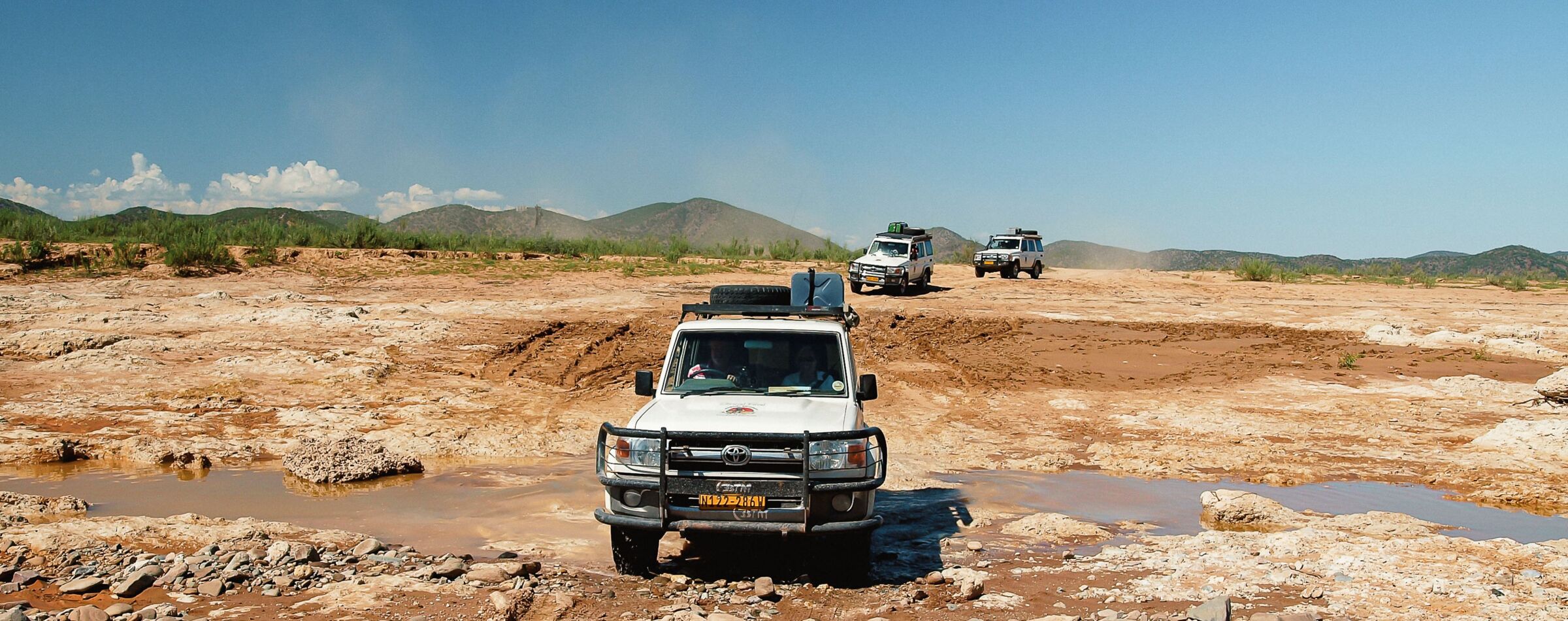 Geländewagen durchquert eine raue Offroad-Strecke in Namibia. Abenteuerreise mit Gravel Travel durch unberührte Wildnis und Flussbetten.