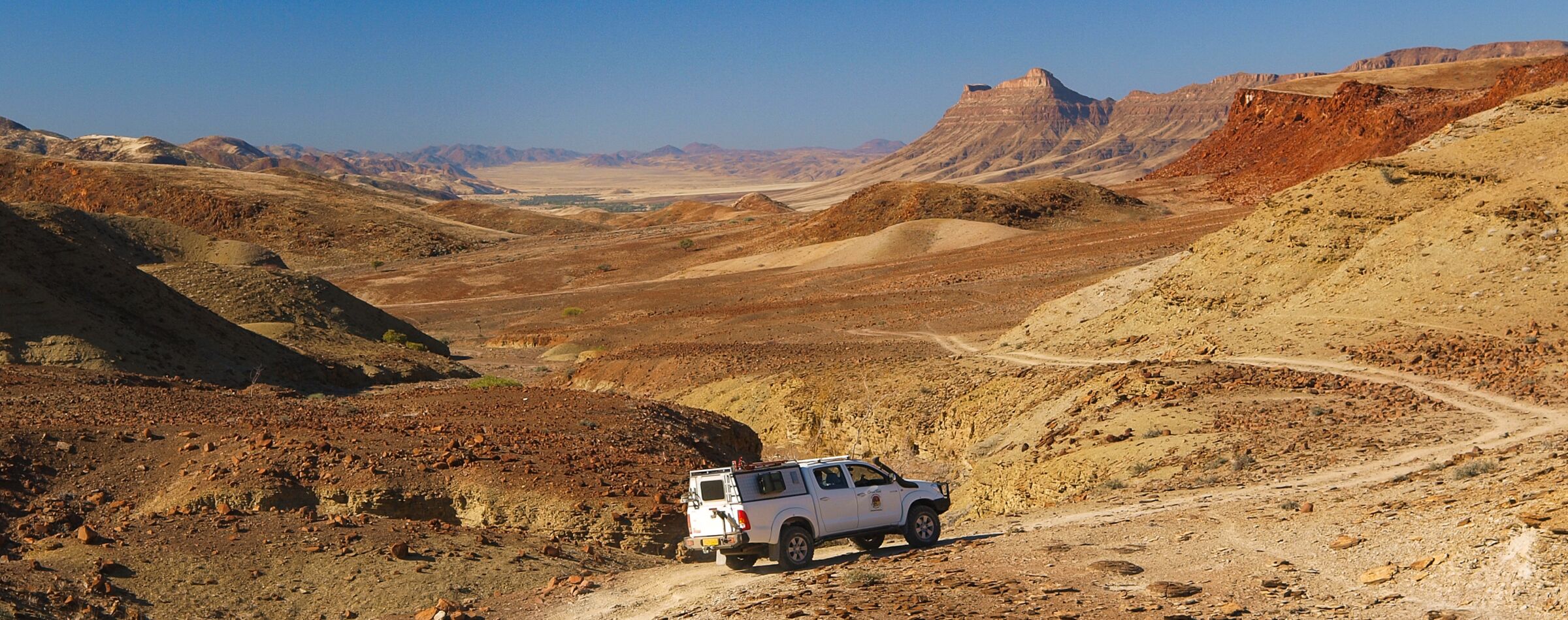 Geländewagen fährt auf einer kurvigen Offroad-Strecke durch die beeindruckende Wüstenlandschaft Namibias. Unberührte Natur mit Gravel Travel erleben.