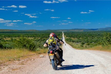 Motorradfahrer auf einer staubigen Offroad-Strecke in Namibia mit weitem Blick auf die Landschaft